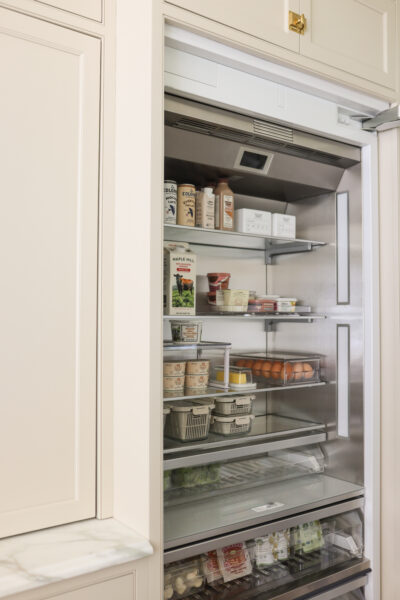 Built-In organized fridge with glass shelves, clear bins, and labeled containers for dairy, eggs, and produce.