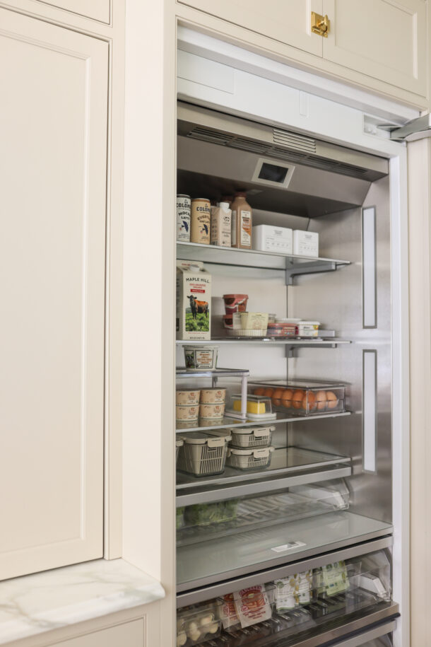 Built-In organized fridge with glass shelves, clear bins, and labeled containers for dairy, eggs, and produce.