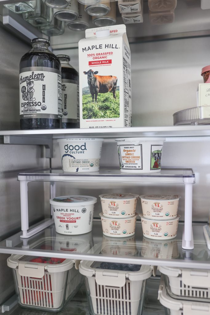 Fridge shelves with cold brew, milk, cottage cheese, and yogurt cups organized on a riser above bins of berries.