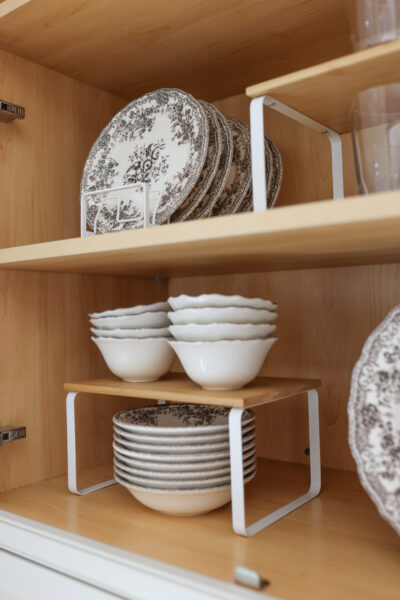 Cabinet organized with vintage floral plates and bowls in wire plate racks, plus a stackable riser shelf holding drinking glasses