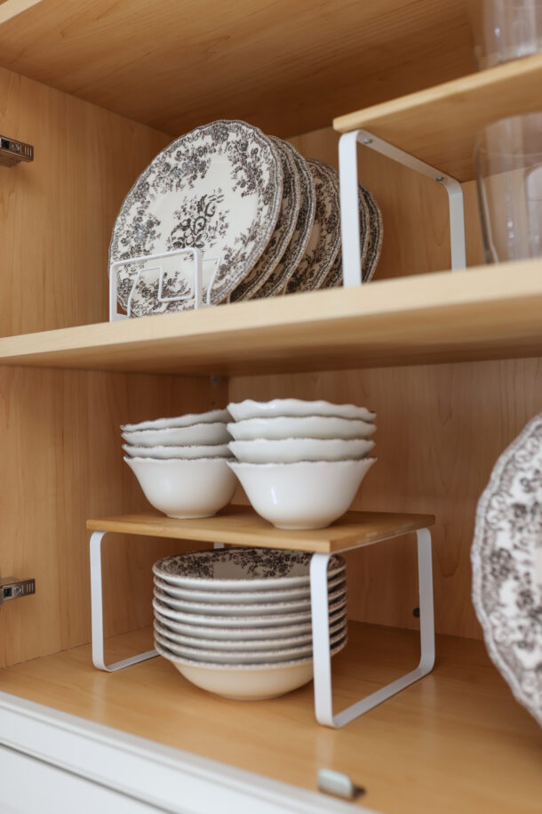 Cabinet organized with vintage floral plates and bowls in wire plate racks, plus a stackable riser shelf holding drinking glasses