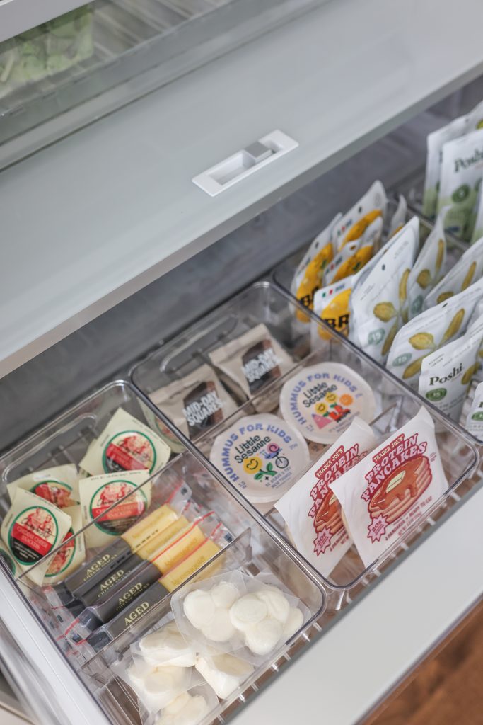 Fridge drawer with divided bins sorting individual snacks like cheese, kids' hummus, and protein pancakes.